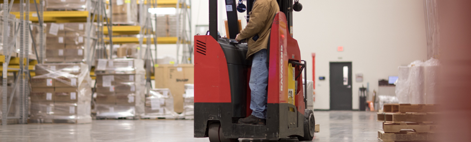 A worker drives a red forklift in a warehouse