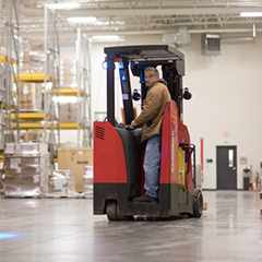 A worker drives a red forklift in a warehouse