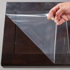 A surface protection film is being removed from a wooden cabinet door.